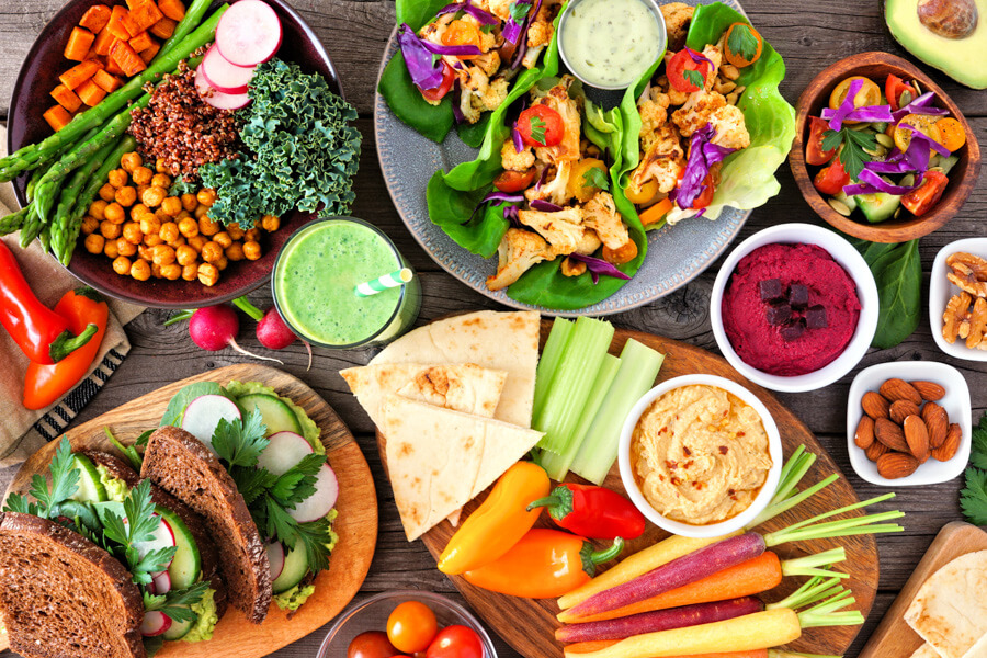 A vibrant, top-down spread of healthy, colorful, wholesome food and fresh ingredients, including hummus, vegetables, bread, and grains, representing nourishing wellness brunch.