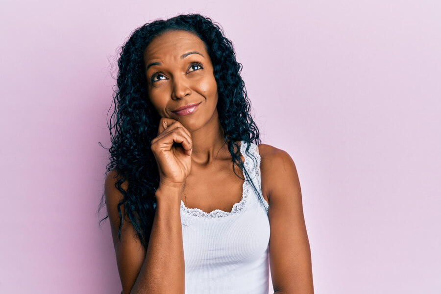 A woman with long dark, curly hair looking up thoughtfully with her finger on her chin, representing reflection, problem-solving, and inner clarity.