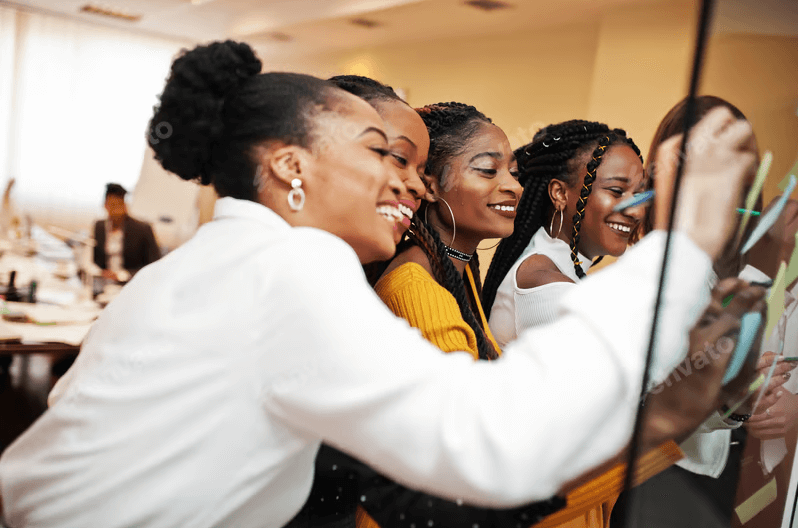 Diverse group of women smiling and collaboratively writing or working on a whiteboard during a workshop or group discussion, emphasizing connection and learning.